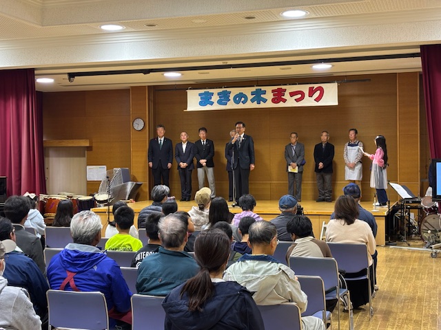 壇上で挨拶する市長と後ろに立っている来賓の男性5人、座って話を聞く多数の来場者