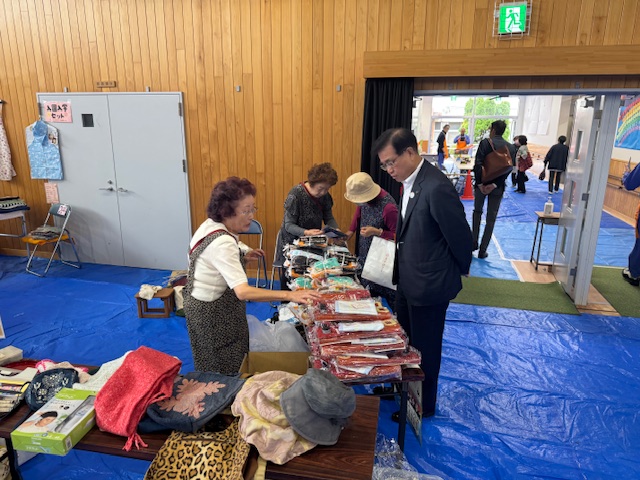 フリーマーケットで展示品を見て売り場の女性と話しをする市長
