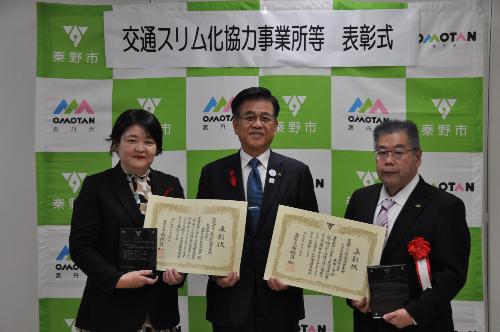 表彰状を持った男性と女性の間に市長が立っている写真