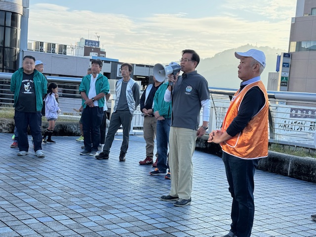 拡声器を持って話をする市長とその周辺に役員のジャンバーを着た男性数名