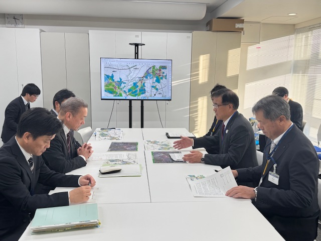 テーブルをはさんで向かい合うスーツの男性8名