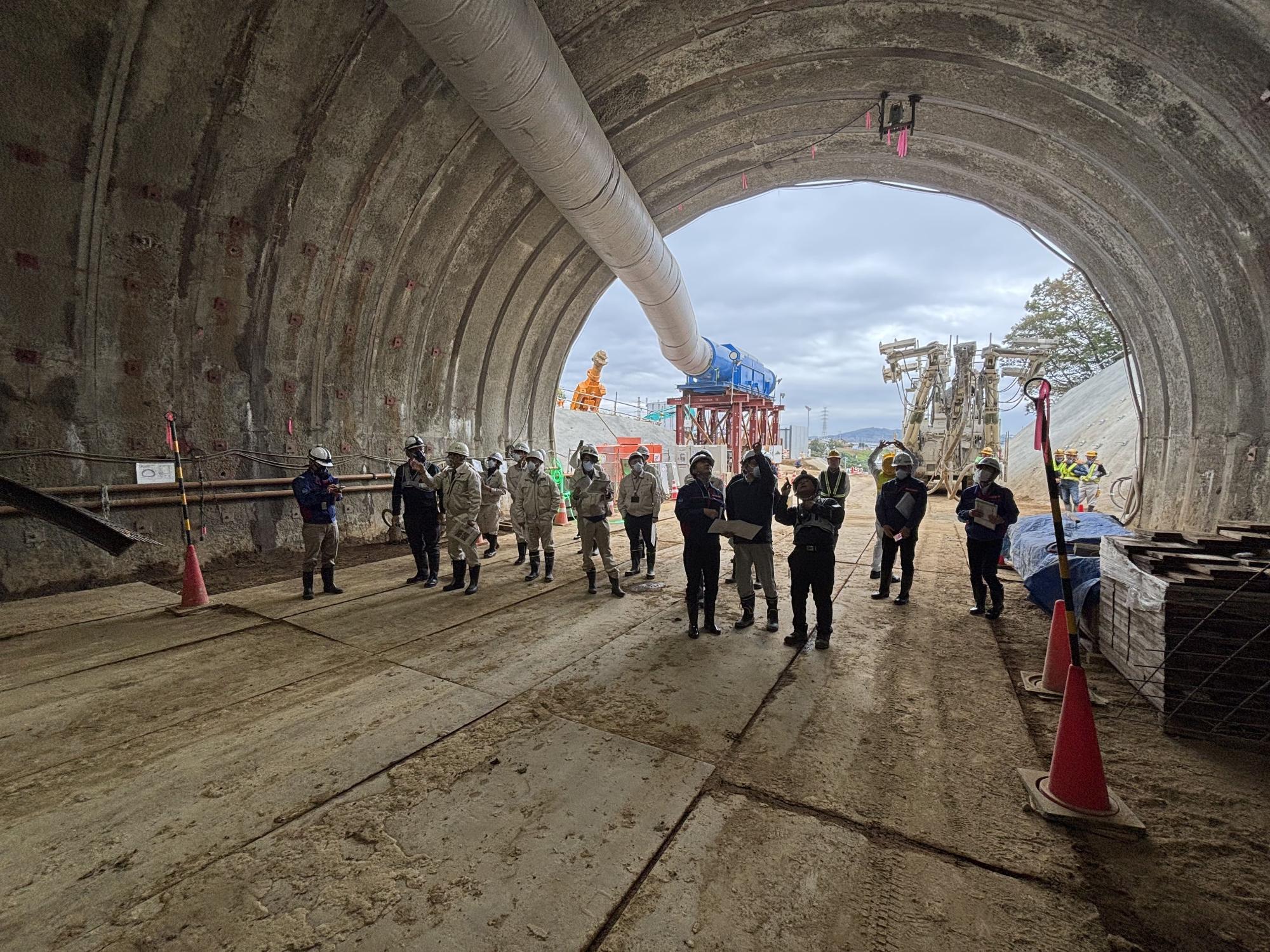 作業着姿の男性がトンネル内部を見学する様子をトンネルの中から写した写真