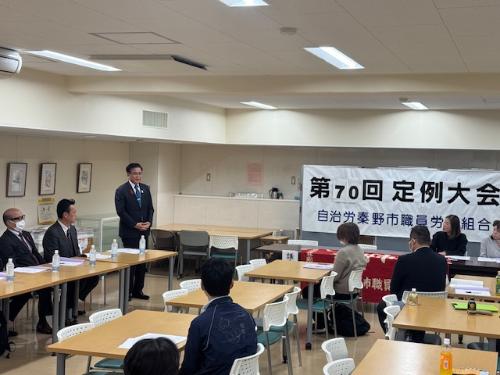 テーブルに数人の人が集まっている会議室で挨拶する市長