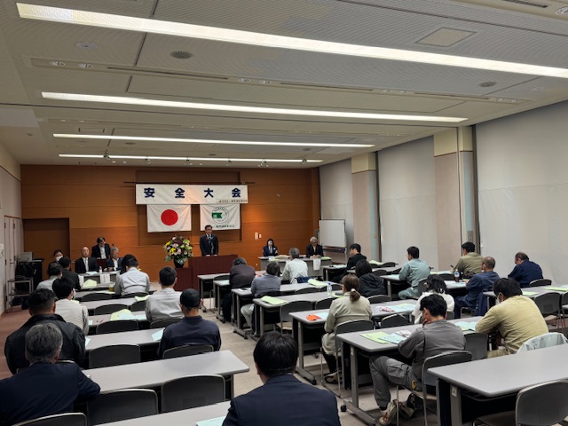 会議室に2人ずつ着席した机が3列7台ずつ並んでいる。奥に挨拶する市長。