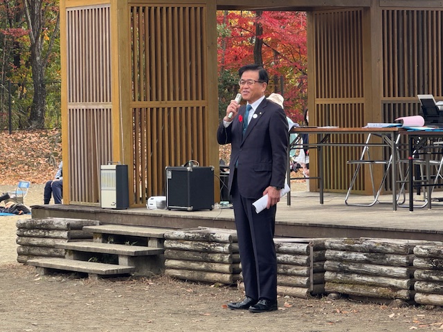 屋外の木造建物の前で挨拶する市長