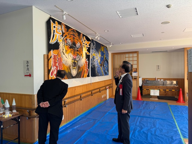 壁に掛けられた大きな絵を見学する市長とスーツの男性1人