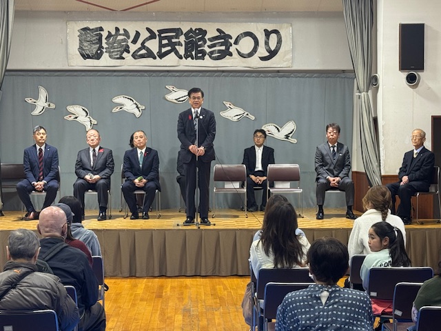 壇上で挨拶する市長とその後ろに座る5名の来賓、手前にはいすに座る多数の来場者