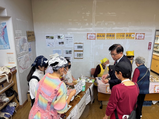 模擬店を見学する市長と売り物を照会する女子中学生3人