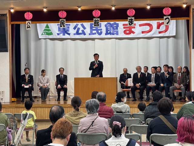 椅子に座る多数の来場者の前で挨拶をする市長とその左右に来賓が座っている。