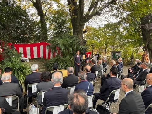 紅白の幕の前で挨拶する市長とその前に座る多くのスーツの男性