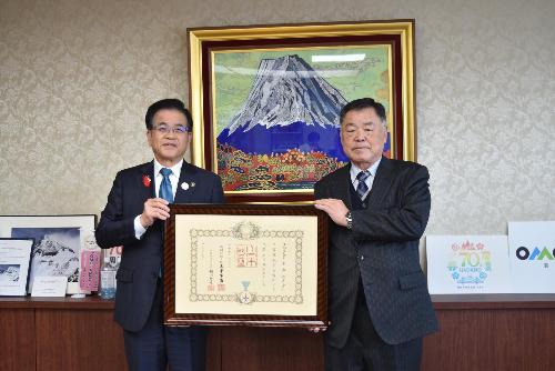 富士山の絵の前で市長と受賞者が表彰状を一緒に持って立っている