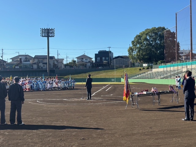 野球のマウンド近くで挨拶する市長と、奥にユニフォームを着た子供たちが大勢整列している