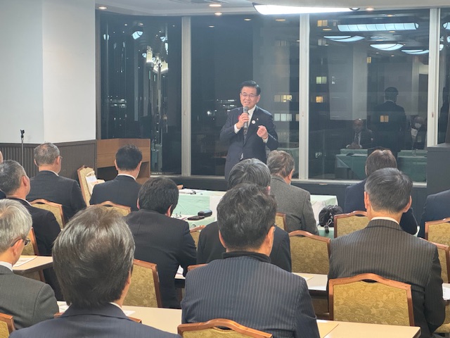 椅子に座ったスーツの男性たちの前で講演する市長