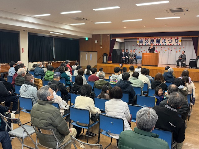 椅子に座った大勢の老若男女の奥のステージ上で市長が挨拶をしている。