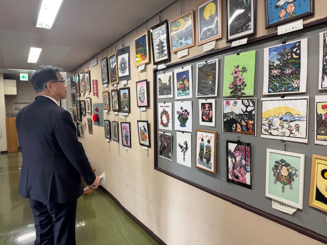 壁一面に展示された絵などの作品を見学する市長の後ろ姿