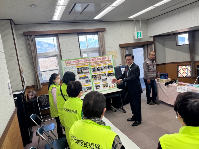 渋沢地区民児協のジャンバーを着た5人のの女性と談笑する市長