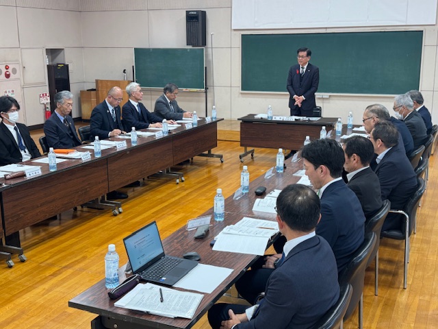 ロの字型の会議室でスーツの男性が会議をしている様子を斜めから撮った写真