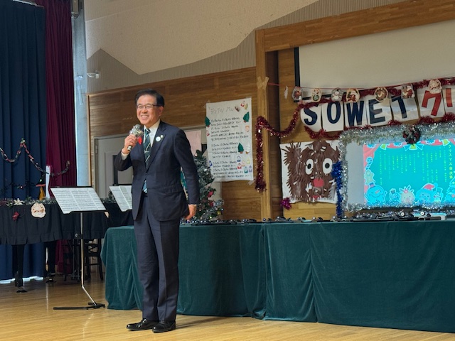 クリスマスの装飾のある部屋で市長が立って挨拶をしている