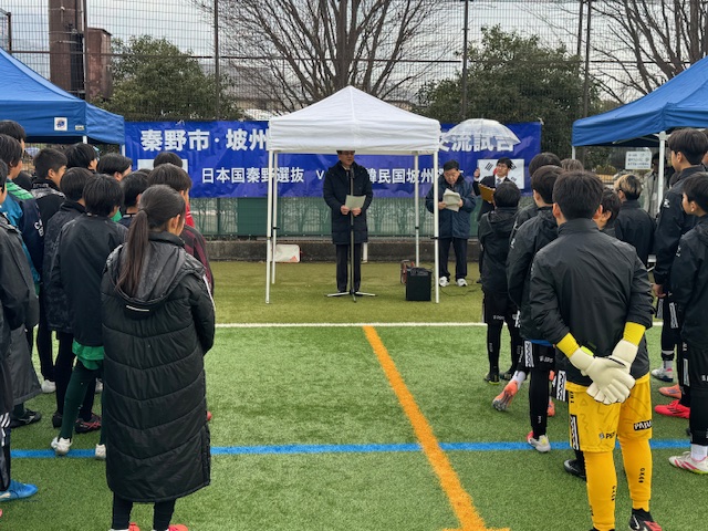 小さなテントの下で市長が挨拶をし、ジャージに上着を着た子供たちが聞いている。