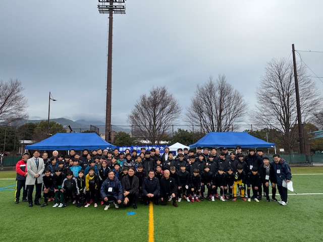 厚い曇の立ち込めた空の下で集合写真を撮る少年少女と市長