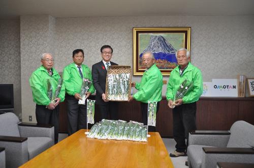 緑のジャンバーを着た4人の生産者の男性が市長を囲んで立っている。手には葉ニンニクを多数カゴに入れている