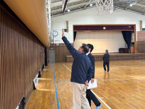 小学校の体育館に設置された空調設備を指さす市長。