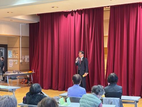 大きな赤い幕の前で立ってマイクを持ち挨拶をする市長