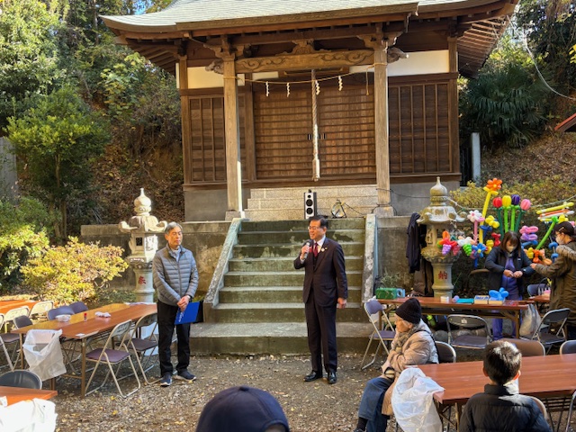 屋外のお堂の前でマイクを持って挨拶する市長