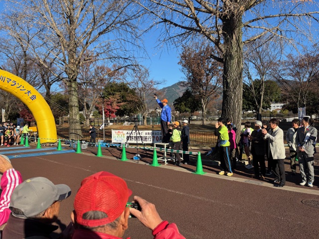 青いジャンバーにオレンジのキャップをかぶった市長が、ピストルを掲げてスタートの合図をしている。