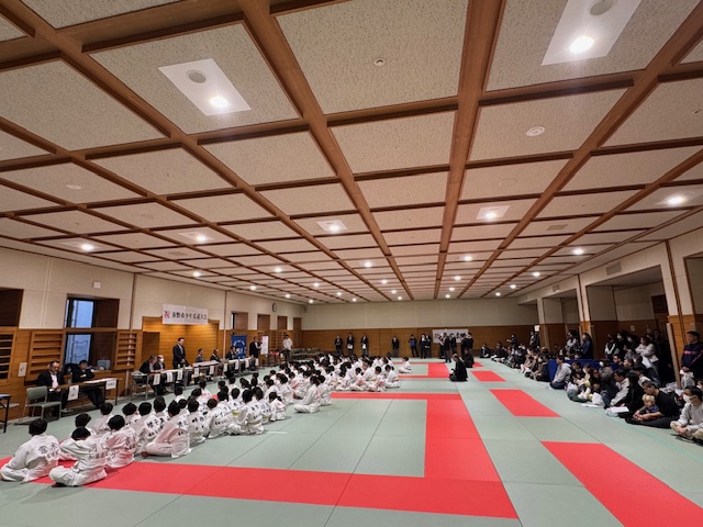 縦に長い柔道場で柔道着の少年しょす所が多数座っている