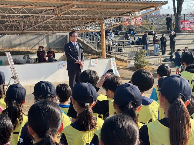 陸上競技場で大勢の子どもたちの前で挨拶する市長