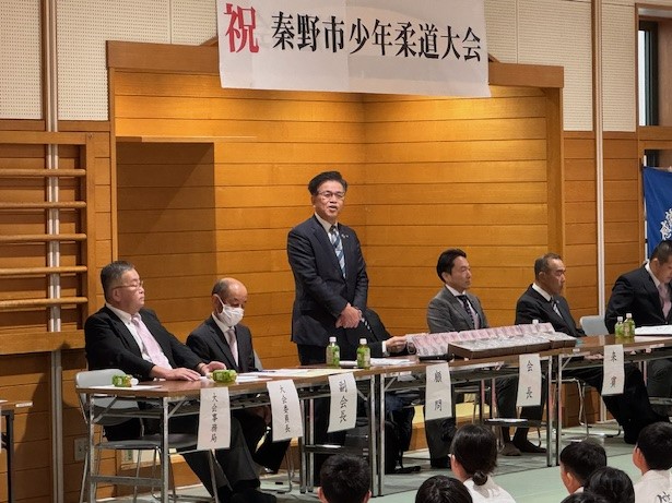 立って挨拶する市長の左に主催者の男性2名、右に来賓の男性3名が座る。