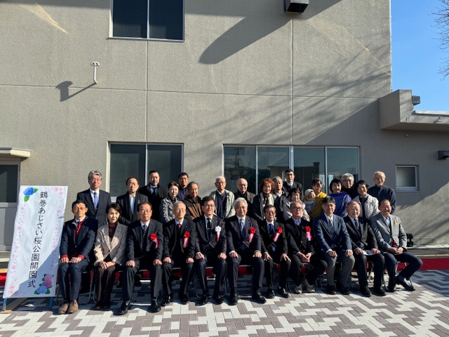 屋外で前列に12人が座り、後列に20人ほどが立って集合写真を撮っている。