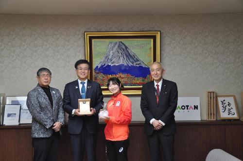 中央に市長と女性選手がそれぞれメダルと記念品を持ち、その両端にスーツの男性が立っている