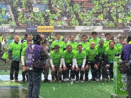 雪の降るサッカーコートで2列に並んで写真を撮るユニフォーム姿の男性20名