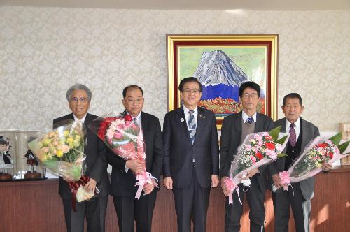 市長を中心に、左右にスーツの男性が2人ずつ、それぞれバラとカーネーションの花束を持って立っている。