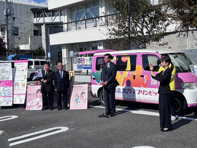 ピンク色のデフリンピックキャラバンカーの前で挨拶する市長と手話通訳者