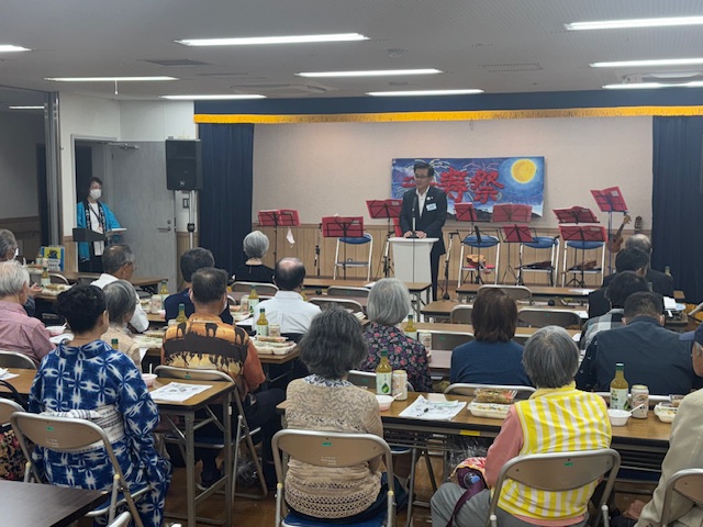 老人ホームで挨拶する市長とそれを聞く多数の高齢者