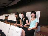 傍聴席に座っている3人の女性のうち、通路側に座っている女性が人差し指を立てて口の前に添え、静かにするポーズをしている写真