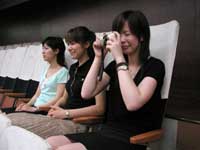 傍聴席に3人の若い女性が横に並んで座り、一番手前の黒い服の女性がデジタルカメラを構えて本会議を撮影しようとしている様子の写真