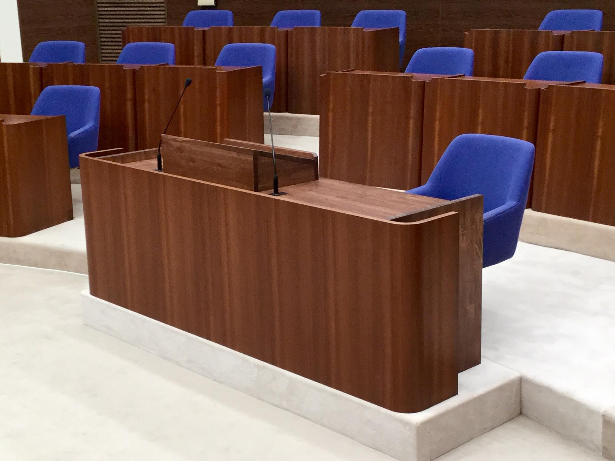 木製の演壇と青い椅子が整然と並ぶ議場の内部で、発言用マイクが設置された質問者席が中央にある写真