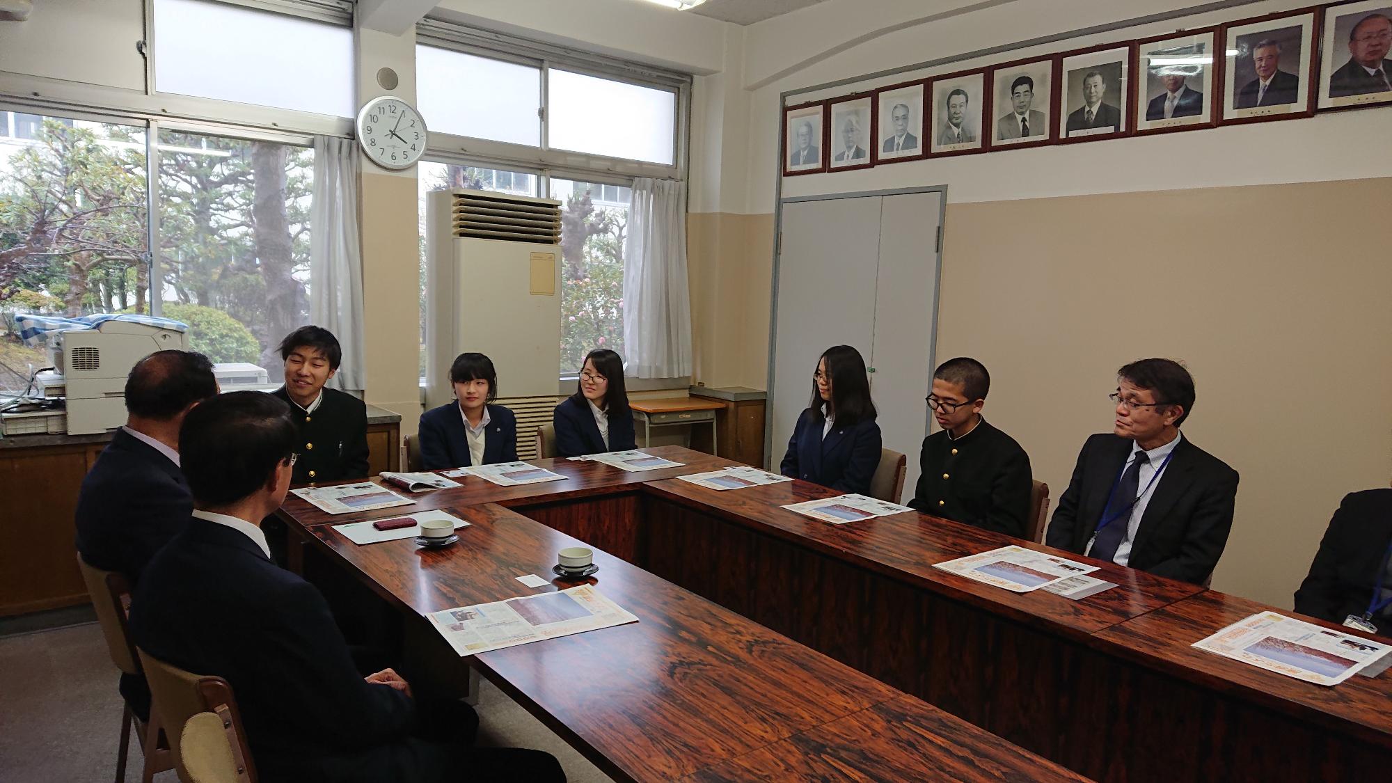 応接室の大きな木製のテーブルを囲んで座るスーツ姿の正・副委員長と懇談する写真部の部員たちの写真