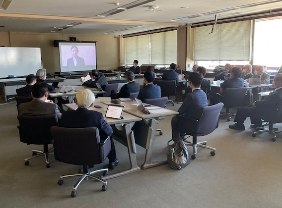 会議室で大勢の聴講者が長机の席に座り、スクリーンに映し出された映像を見ながら、研修を受けている様子の写真