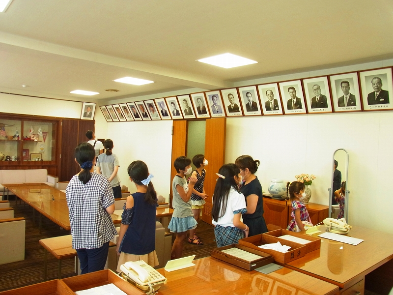 肖像画や写真が多数飾られた部屋で、複数の子供と大人が見学しており、和やかな雰囲気の中で議会を見学をしている様子の写真