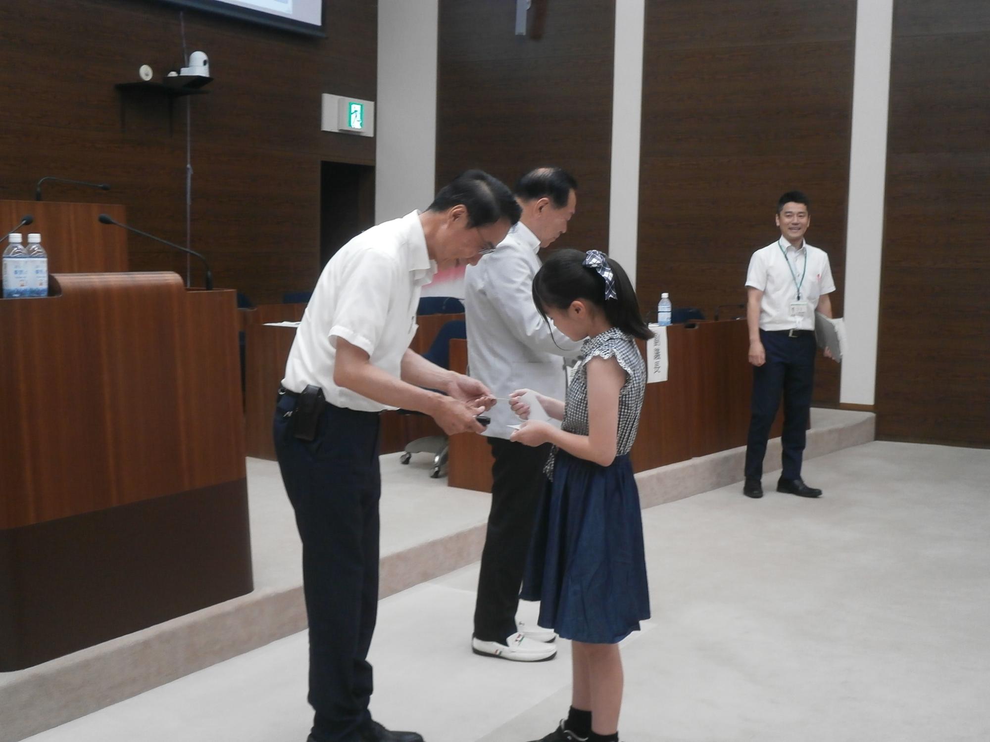 夏休み子ども議場見学会にて、子どもが議会関係者から名刺を受け取る様子の写真