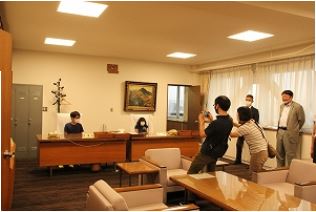 二人の子どもが議長席に座り、その様子を保護者や関係者が写真撮影している写真