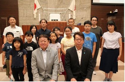 正面中央にスーツ姿の正副議長が椅子に座り、その後ろに子どもと保護者らが整列して笑顔でカメラを見ている集合写真