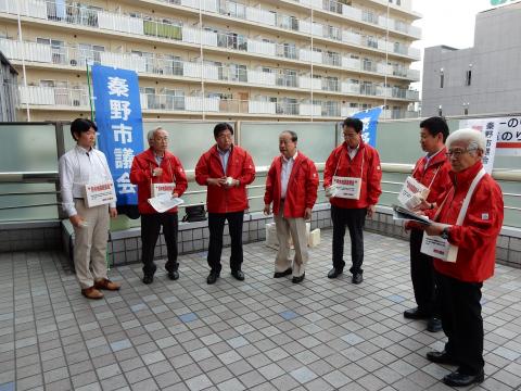 赤いジャンパーと青い「秦野市議会」ののぼりを背景に、7人が何かの募金活動を行なっている風景を捉えた集合写真