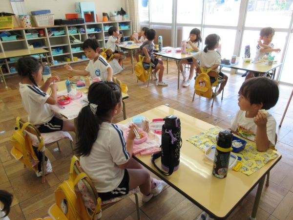 教室で、複数の園児たちがテーブルに座り、それぞれお弁当を広げてランチを楽しんでいる写真
