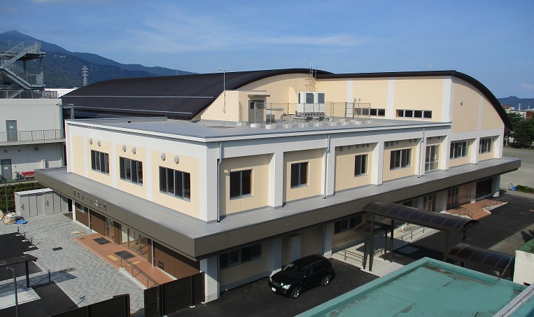 淡い黄色の壁と茶色の屋根を持つ体育館の全体を写した外観写真